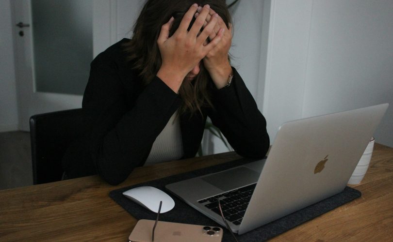 a woman covering her face while looking at a laptop